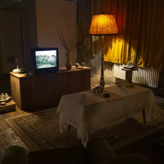 A dimly lit room containing a TV and lamp staged for "The Neighbours"