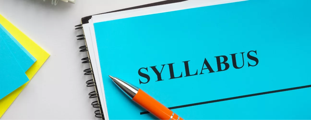 A blue page with a header that reads "syllabus" on a desk with a pen. 