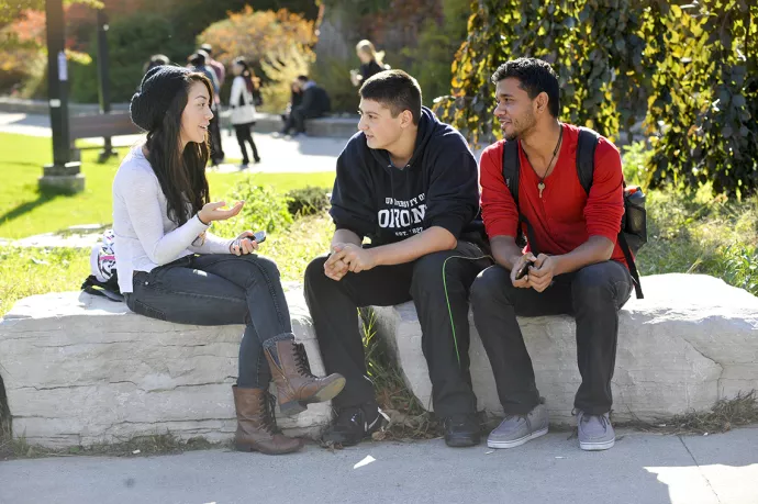 three students chatting while sitting outside on rocks