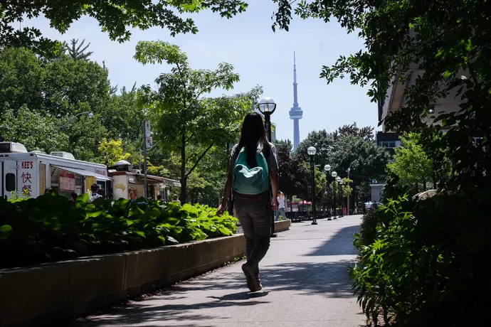 female student with backpack walking along sidewalk with CN Tower in background