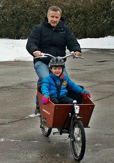 Man riding a cargo bike with a young boy in the cargo box