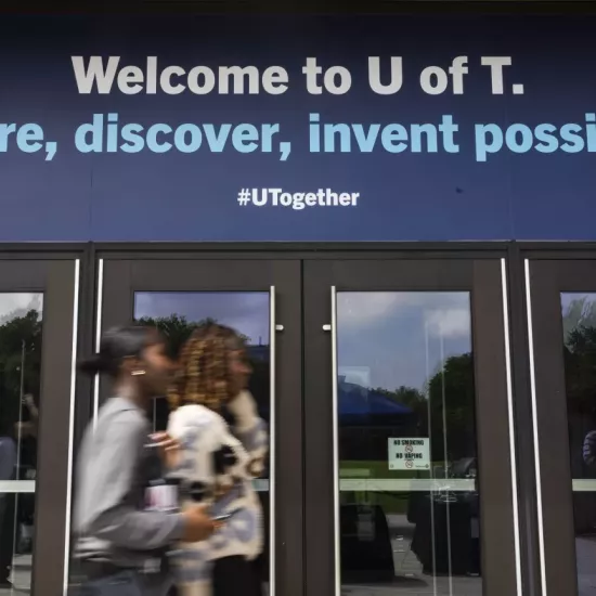 2 black students walking past front doors. Sign above says Welcome to UofT. Explore, discover, invent possibility.