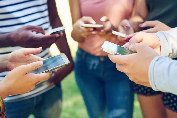 A circle of teenagers in a field using their cellphones