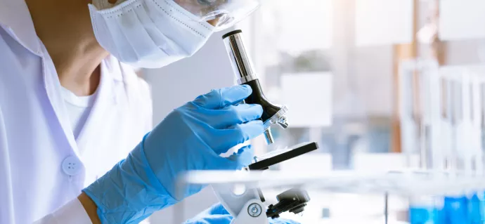 Scientist wearing safety equipment looks into a microscope