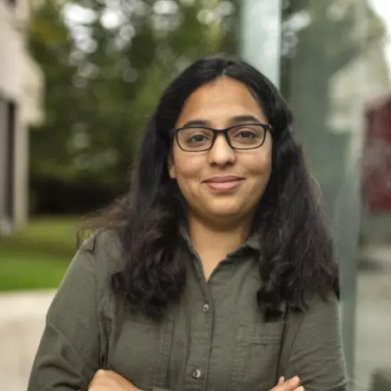 nehal naik smiling with her arms crossed, wearing a dark green button up. She has shoulder length brown hair and black glasses with square shaped rims. 