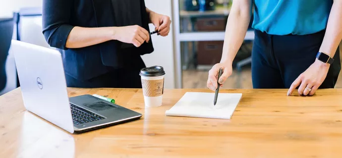 Two professionals referring to a printer paper on a desk. Photo by Amy Hirschi on Unsplash