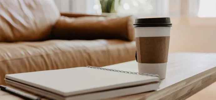 Coffee cup and notebook on coffee table with sofa in background