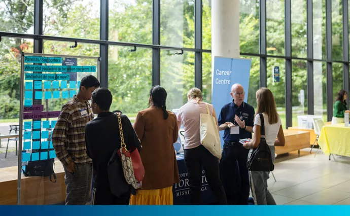 Male staff member chats to students in an atrium