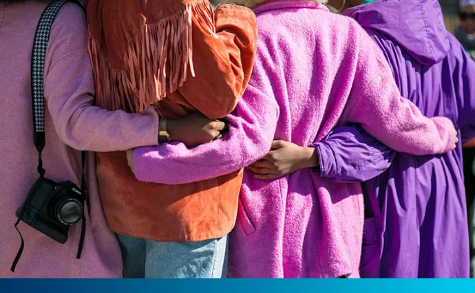 Four women in brightly coloured coats hug