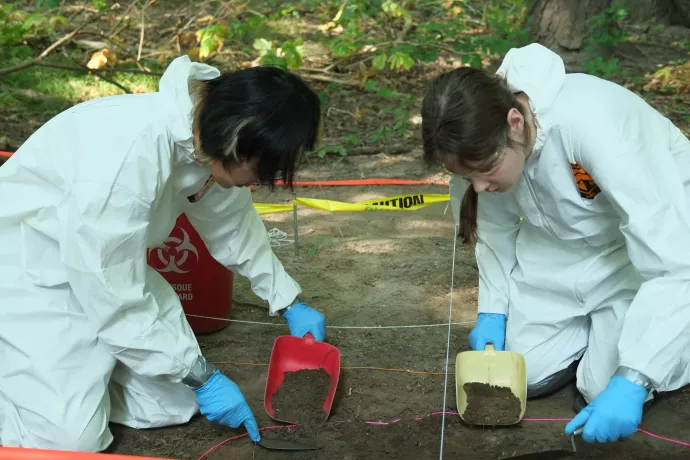 Forensic Field School participants wearing white suits dig through evidence