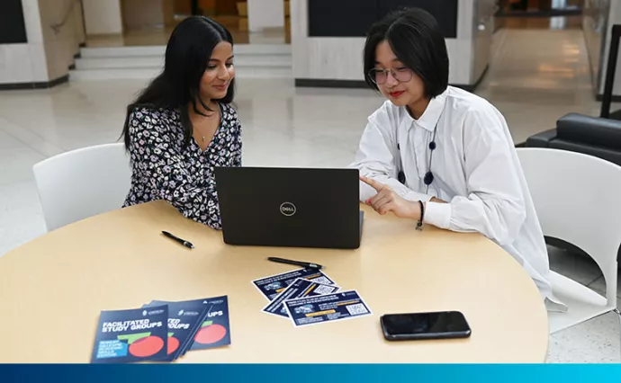 Two women sit and point at a computer screen