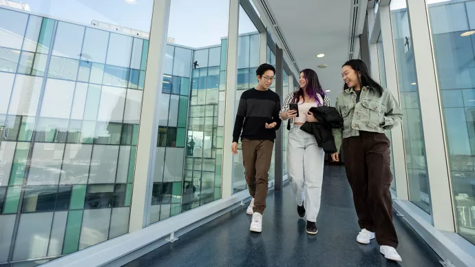 Three students walking along bridge between buildings