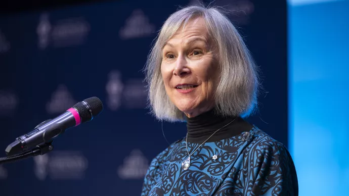 Retired BC Judge Marion Buller stands in front of a microphone, with a blue background