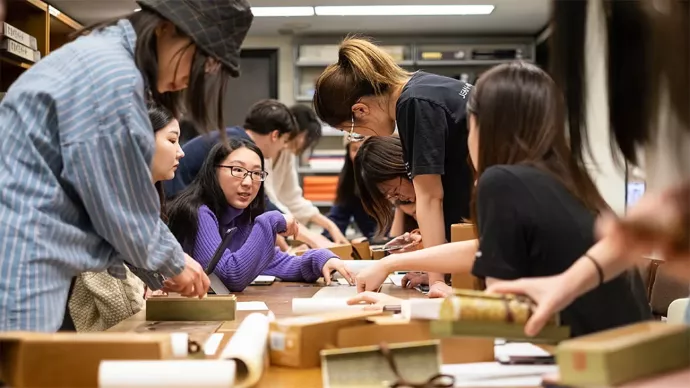 About 10 students surround a table working on what appear to be rolls of parchment