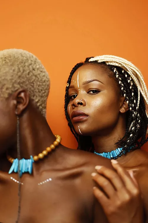 Woman in braids with blue necklace looking over shoulder of another woman with short cropped hair and a blue necklace