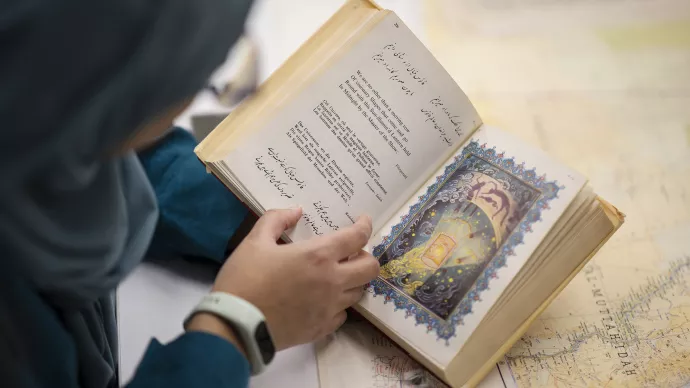 Isra Saymour looks over an old book with text on the left page and a colour image of stars and people on the right