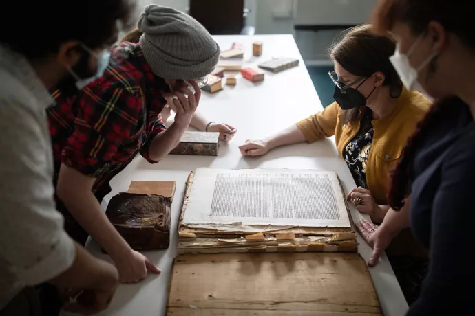 People look at large manuscripts on a wooden table. 