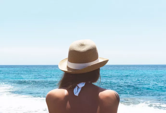 woman wearing a straw hat standing with back to camera looking out over a large body of water on a clear sunny day