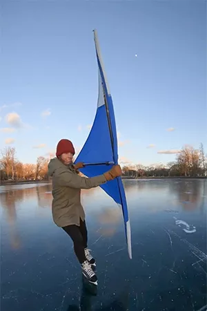 Lisa on ice skates on ice holding a triangular kite sail