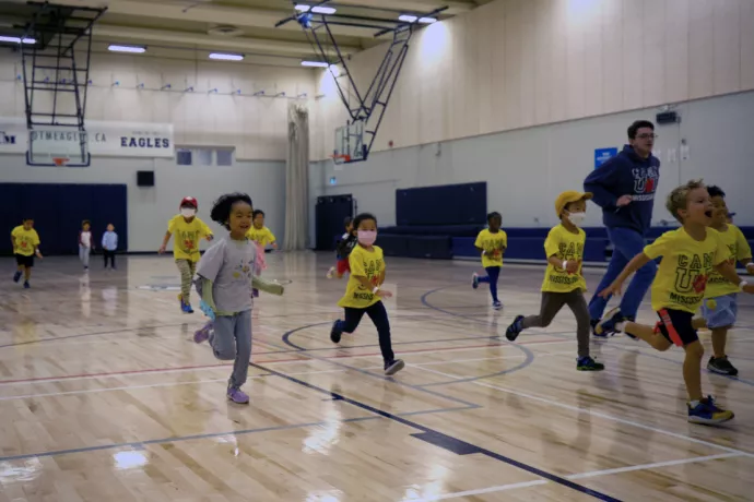 Group of children wearing bright yellow t-shirts running in a gymnasium toward the camera