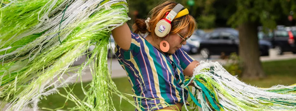 Student with noise cancelling headphones dances with colourful green streamers.