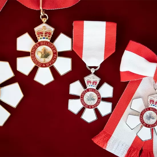 Four Order of Canada medals on a deep red background. Each medal has a white ribbon with a red stripe along both sides.