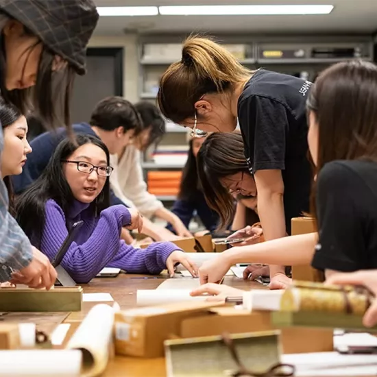 About 10 students surround a table working on what appear to be rolls of parchment