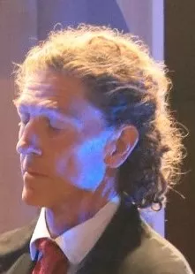 Man with long hair to his  holders wearing a suit and tie on stage