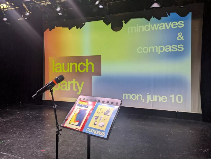 A microphone and lectern stand in front of a projection screen in an auditorium. The slide on the scren reads "Launch Party. Mindwaves & Compass. Mon, June 10."